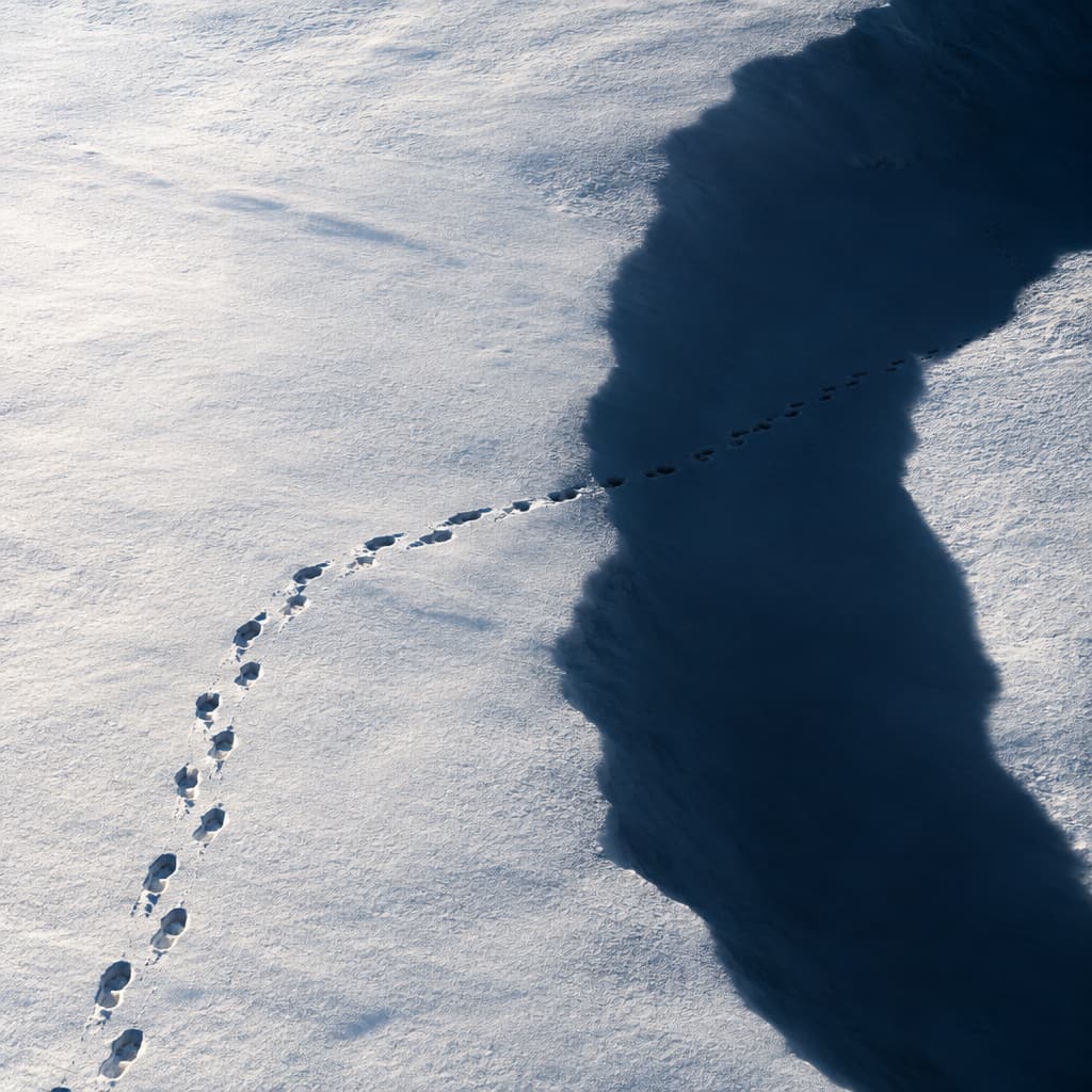 Footprints in the snow reveal flattened ground beneath a shadow that looks like a chasm.